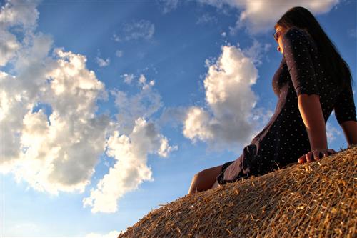 Woman sitting on haystack and watching the sunset